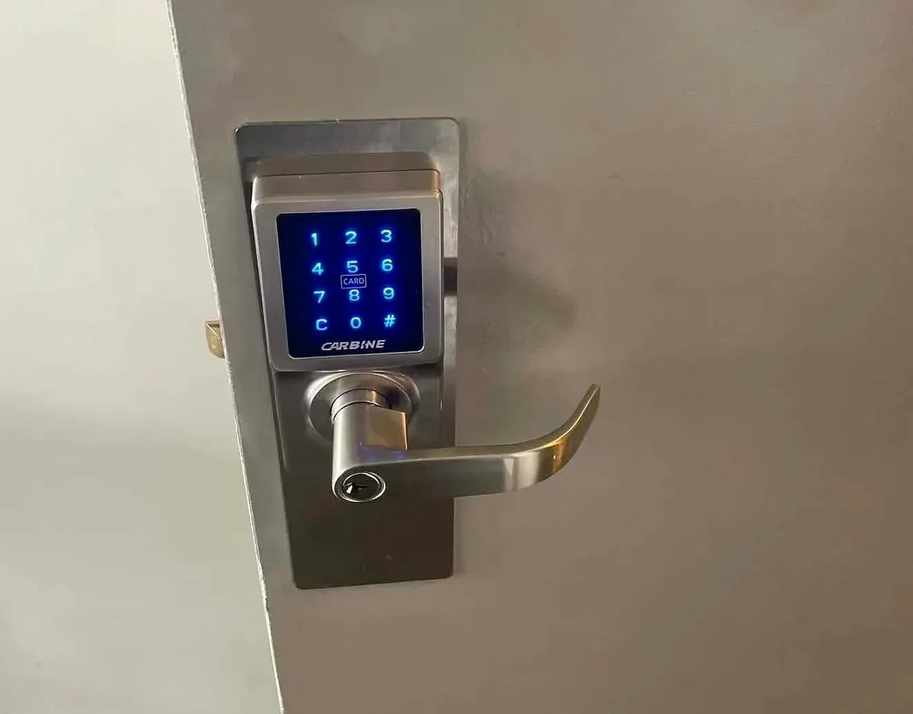 A Carbine keypad and card lever lock lit blue on a grey door, the latch showing at its edge