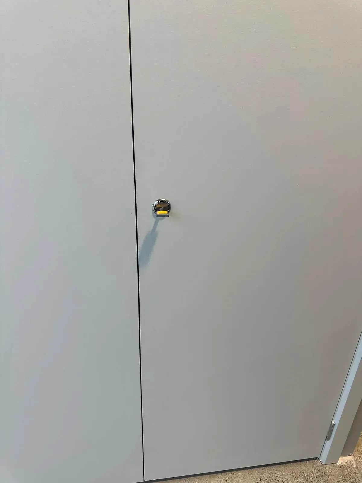 A key with a yellow tag in a flush cylinder lock on a pair of grey commercial doors
