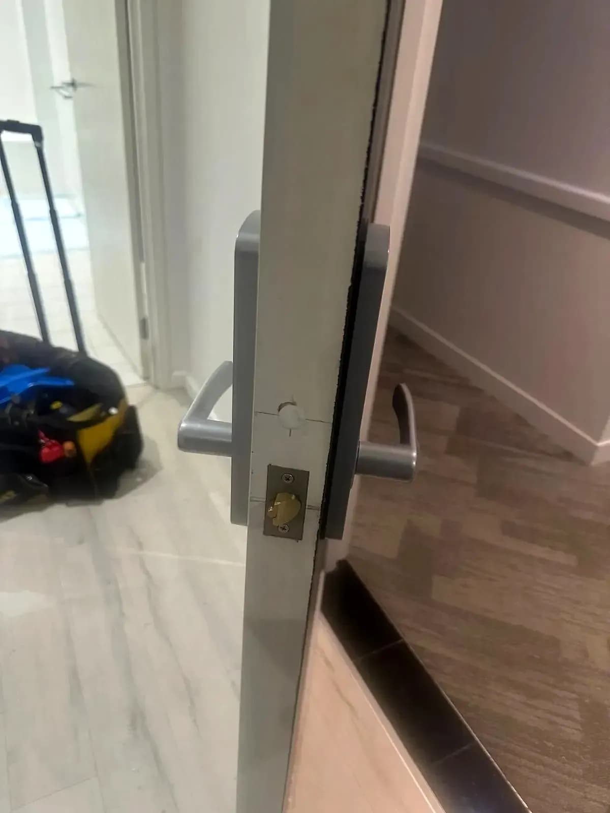 A lever set and latch fitted through a white door in an office corridor, a tool bag on the floor behind