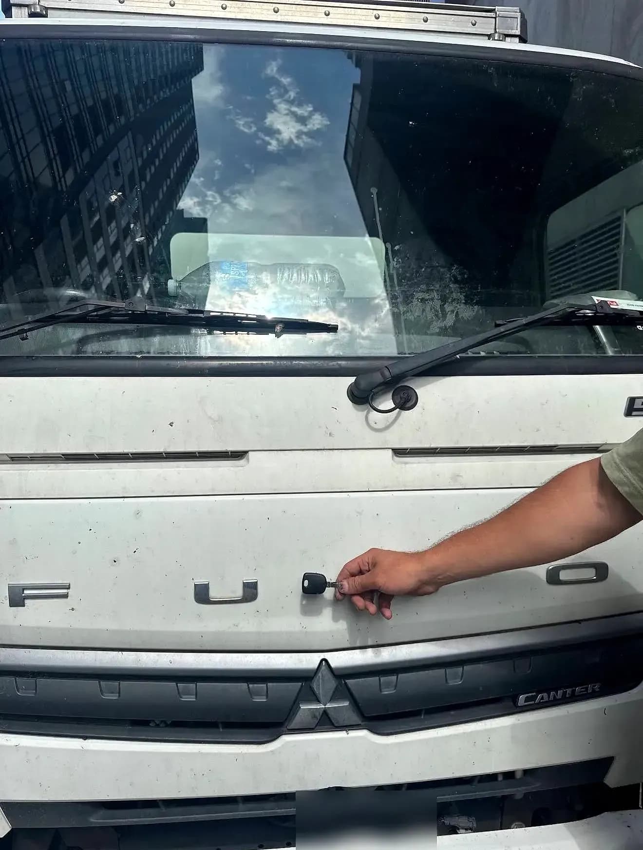 A hand holding a new key up against the FUSO lettering on the cab of a white Mitsubishi Fuso Canter truck