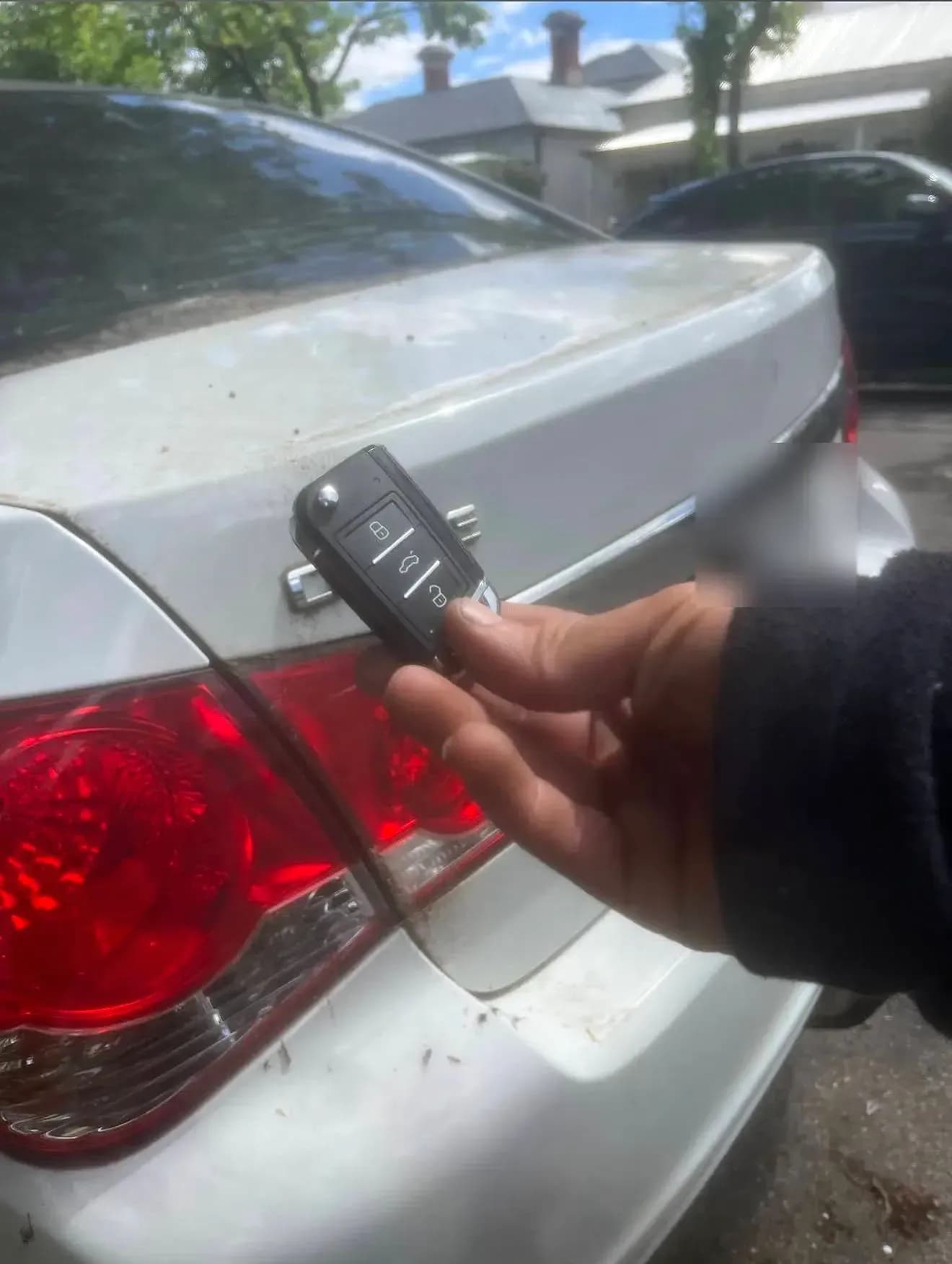 A hand holding a new flip key against the boot of a silver Holden Cruze parked on a suburban street