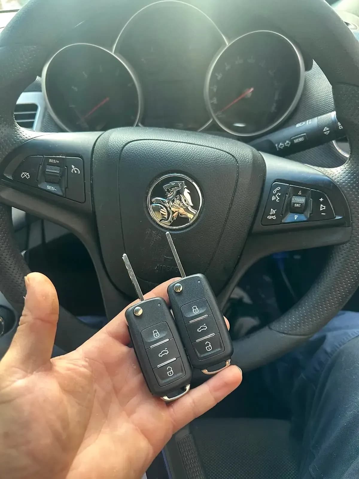 Two new flip keys held in front of the steering wheel of a Holden Cruze