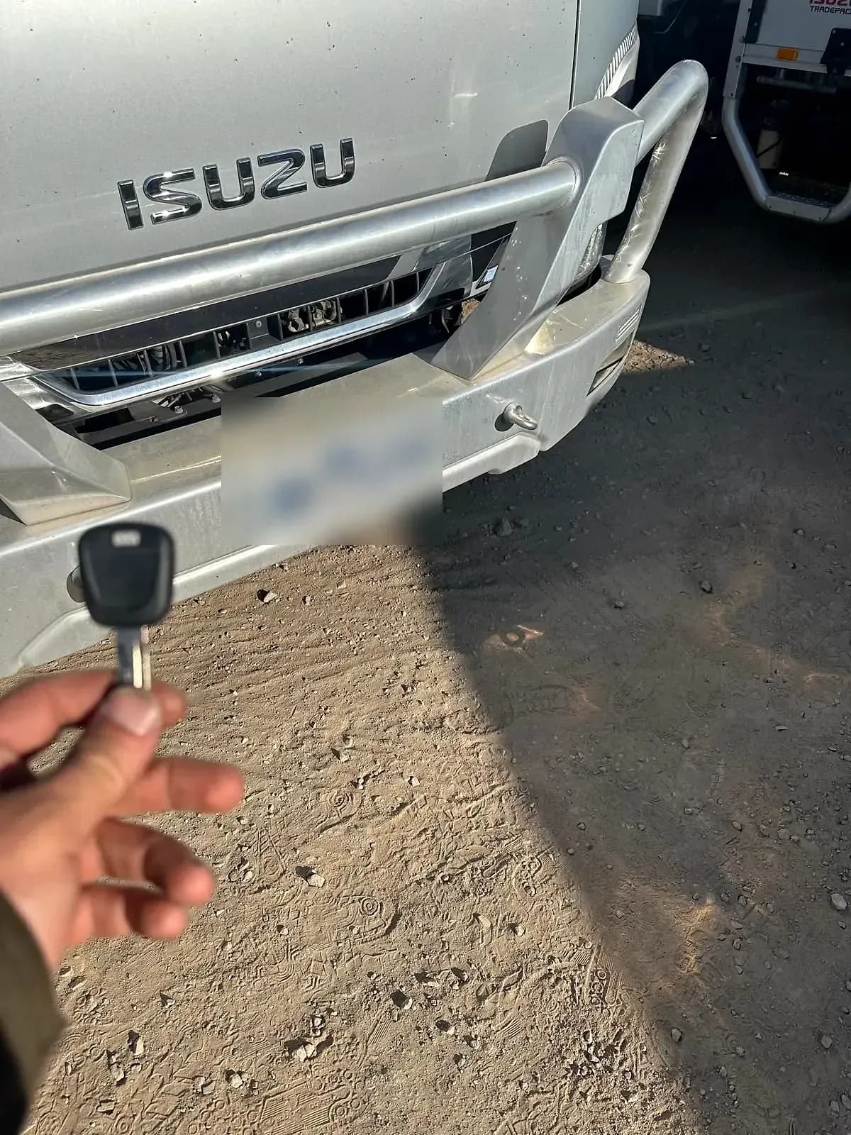 A truck key held up in front of an Isuzu truck, its number plate blurred