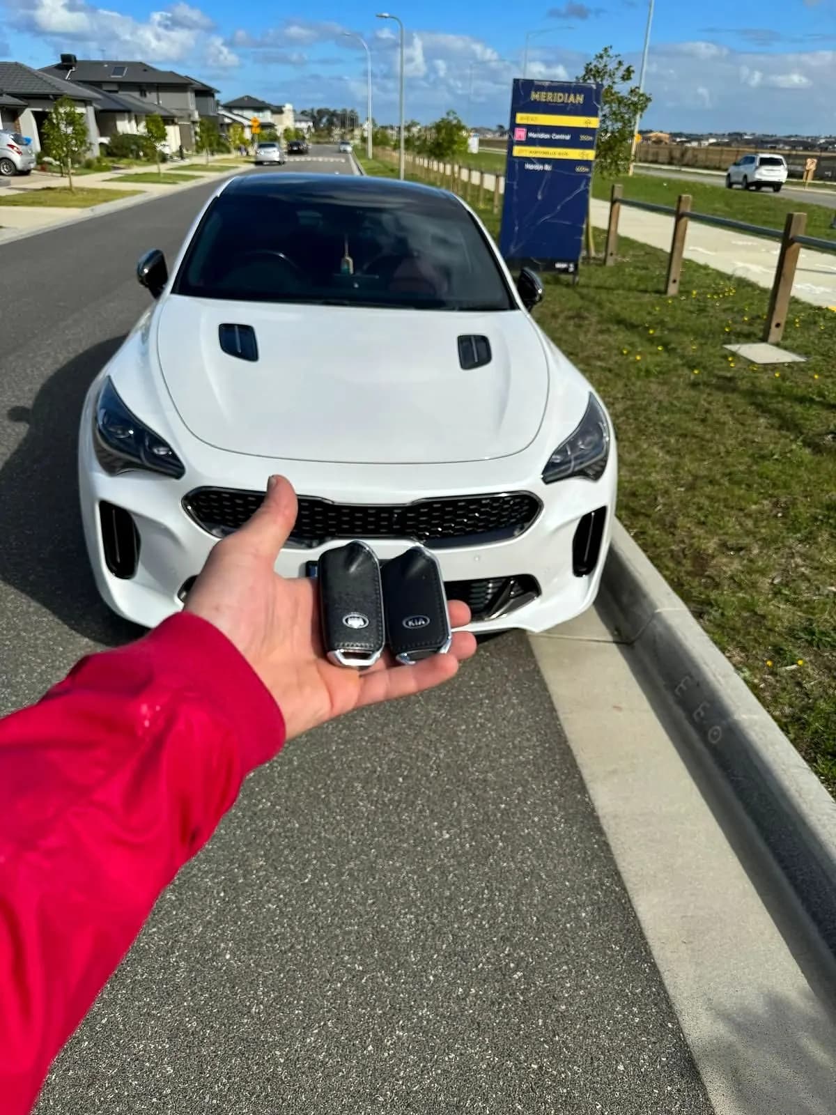 Two smart keys held in an open hand in front of a white Kia Stinger