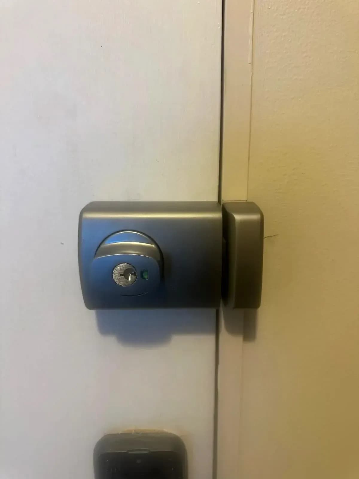 A dark grey rim deadlock with a key cylinder, fitted to a white door beside its frame