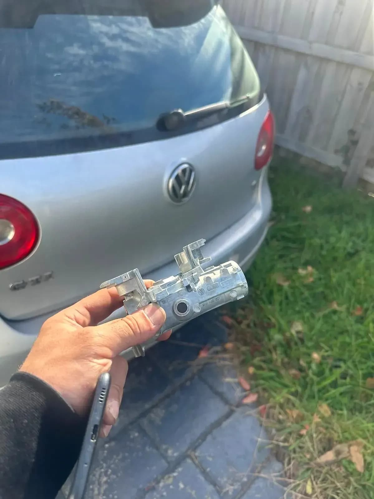 An ignition lock housing taken out of a silver Volkswagen Golf, held up behind the car