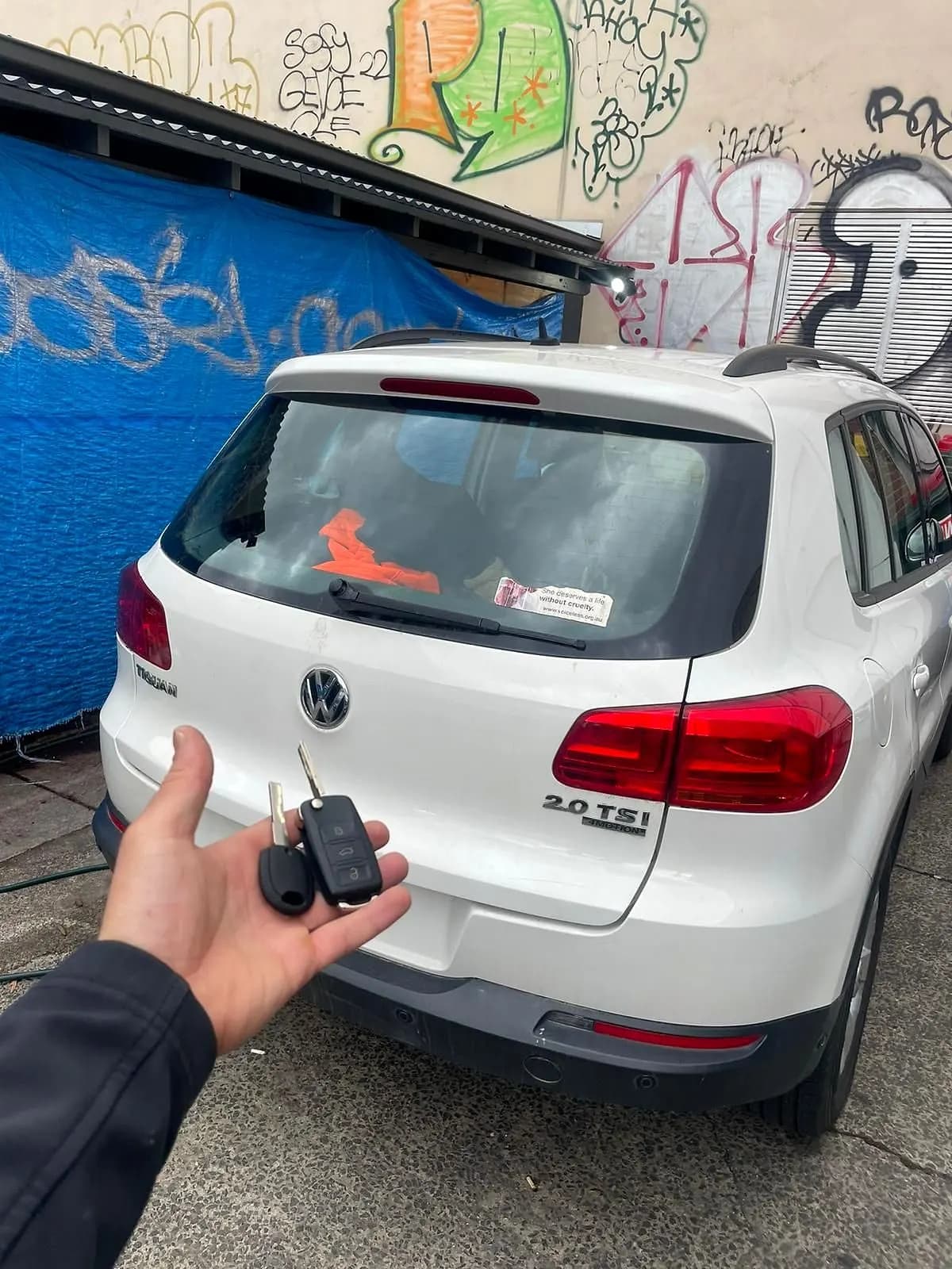 A flip key held in front of the tailgate of a white Volkswagen Tiguan