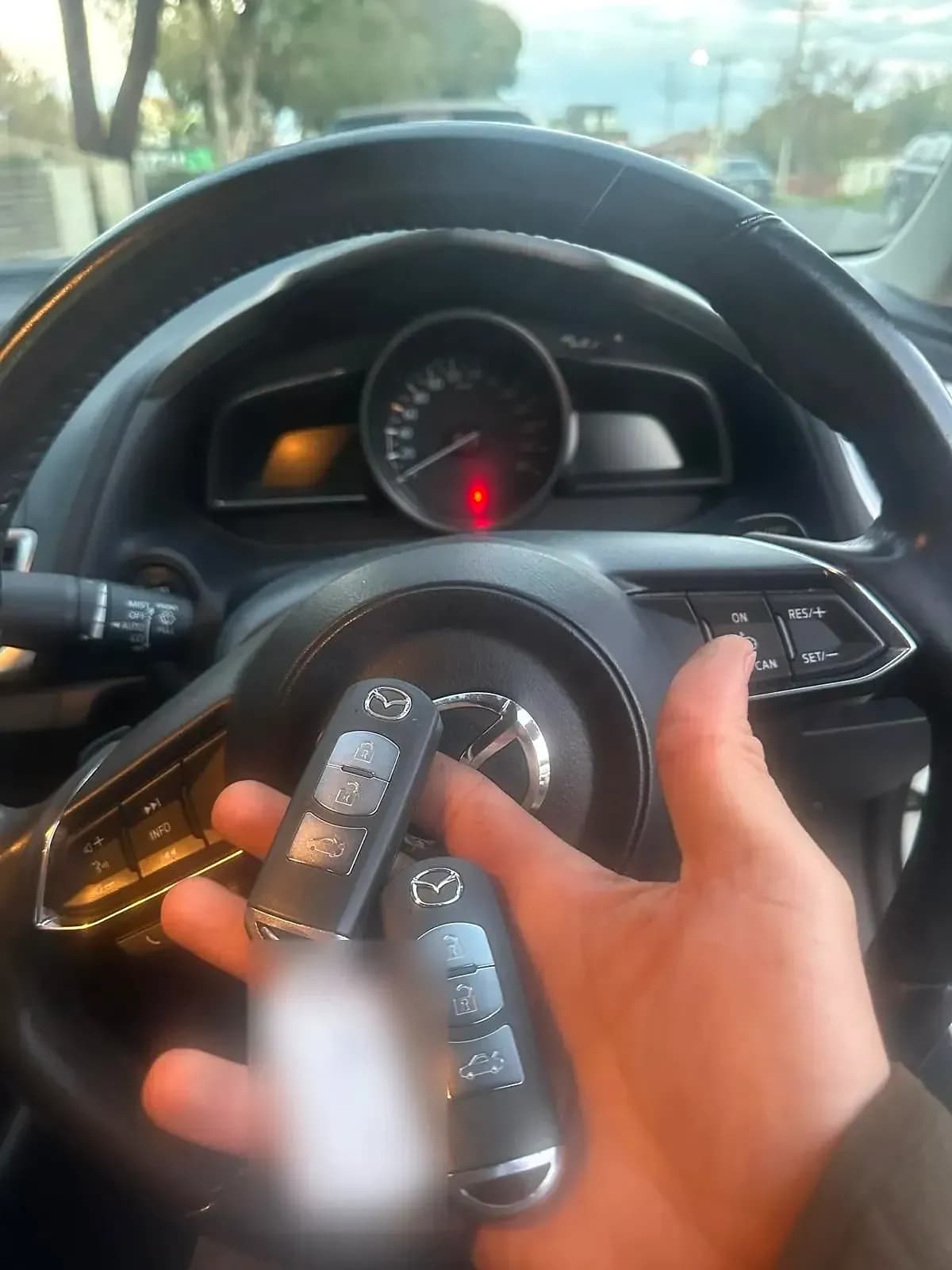 Two Mazda smart keys held in front of the steering wheel of a Mazda, the key tag blurred