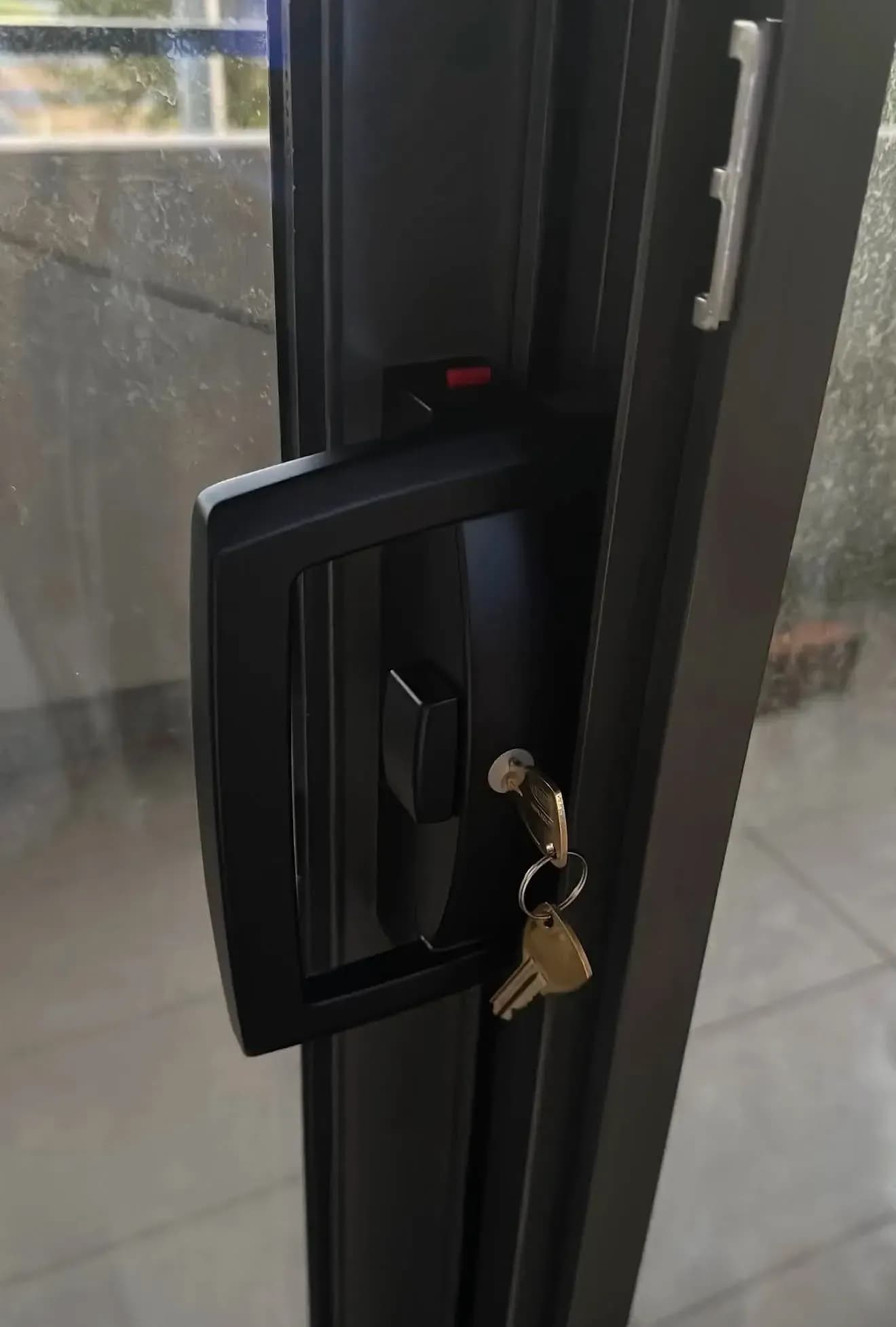 A black keyed handle lock on an aluminium sliding glass door, two new keys hanging from the cylinder
